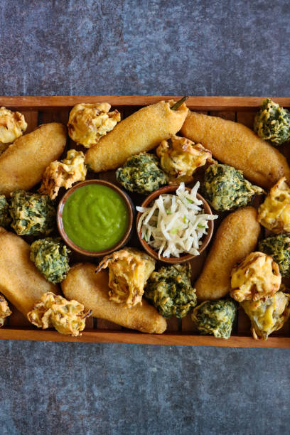 nahaufnahme holztablett mit hausgemachten grünen chili-krapfen (mirch pakora), knusprigen zwiebel-bhajis, palak pakora (spinat-krapfen) schüsseln mit minze und koriander-chutney, geriebenem käse, vegetarischer snack der indischen küche, grauer hintergr - mashed potato food staple vertical color image stock-fotos und bilder