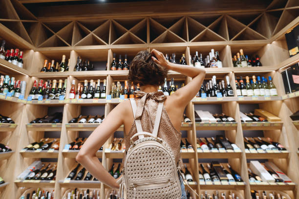 Back view puzzled young woman 20s wear casual clothes shopping at supermaket grocery store buy choosing wine alcohol bottle scratch head inside hypermarket. People purchasing gastronomy food concept. Back view puzzled young woman 20s wear casual clothes shopping at supermaket grocery store buy choosing wine alcohol bottle scratch head inside hypermarket. People purchasing gastronomy food concept alcohol shop stock pictures, royalty-free photos & images