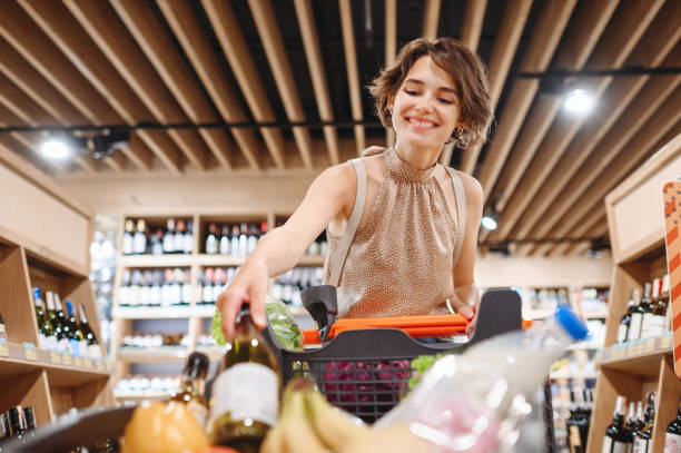 young happy smiling fun satisfied woman in casual clothes shopping at supermaket store hold white wine alcohol put bottle in grocery cart inside hypermarket purchasing gastronomy lifestyle concept. - kundkorg bildbanksfoton och bilder