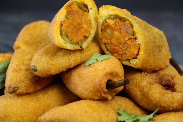 istock Full frame image of pile cooked green chilli fritters (mirch pakora) on a plate, deep fried chilli stuffed with aloo mix (mashed potato, onion and masala), Indian street food, unhealthy eating, grey background, focus on foreground 1371830177