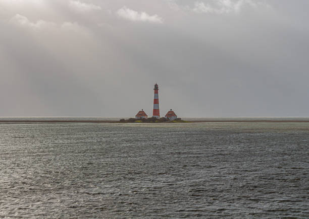 The large lighthouse of Westerhever stands in the middle of the waves of the North Sea after a storm surge in good weather and sun.