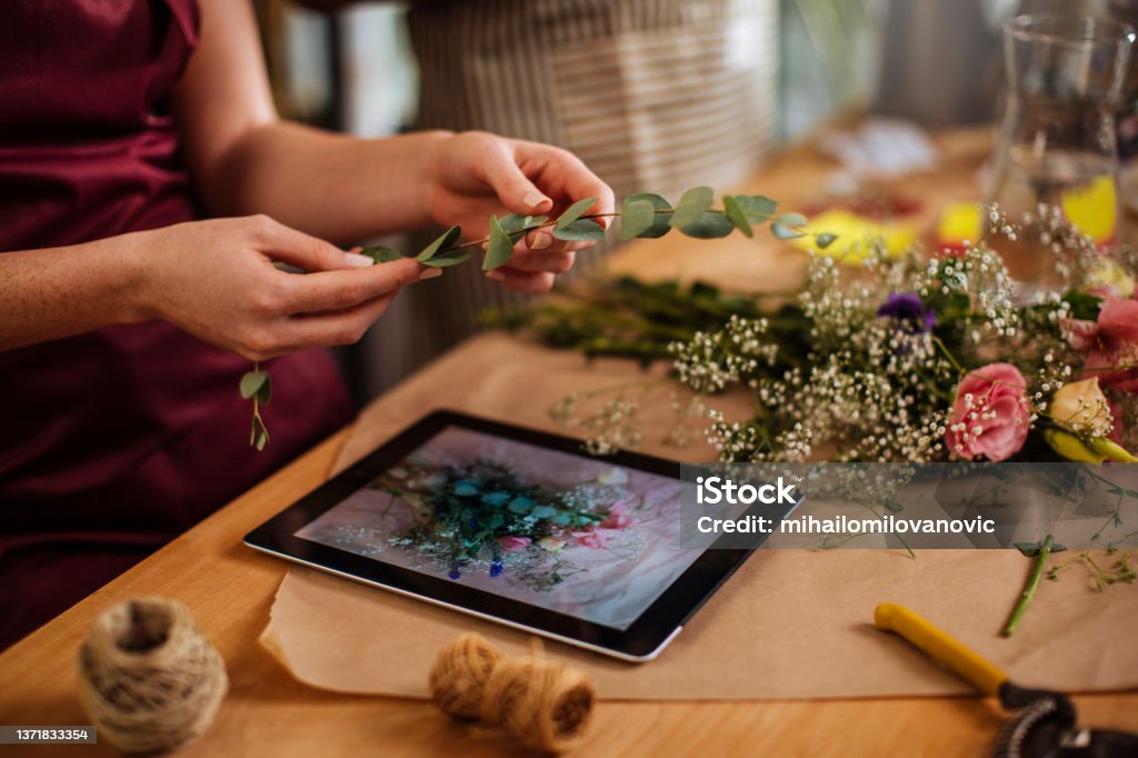 Recreating the image Unrecognizable woman arranging a bouquet while also using a digital tablet Flower Arrangement Stock Photo