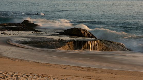 As the waves recede, little waterfalls form on shoreline rocks at Aliso Beach in Laguna Beach, California.