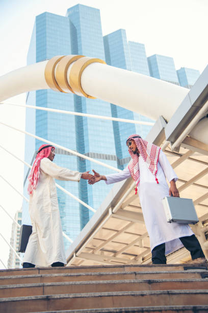 vestito musulmano dell'uomo d'affari arabo che stringe la mano insieme nello sfondo moderno della città degli emirati arabi uniti. uomini musulmani lavoro di squadra stretta di mano partner commerciale con partnership. diversità multirazziale arabo fiduc - sheik abu dhabi united arab emirates asia foto e immagini stock