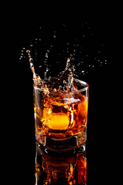 salpicadura de whisky escocés en vaso con hielo natural sobre fondo negro. - whisky fotografías e imágenes de stock