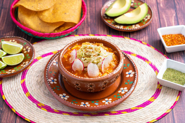 comida tradicional mexicana. sopa de pozole rojo con pollo acompañada de aguacate, lechuga, cebolla, rábano, limón, chile y tortillas crujientes de maíz también conocidas como tostadas sobre fondo de madera. - guacamole avocado mexican culture food fotografías e imágenes de stock