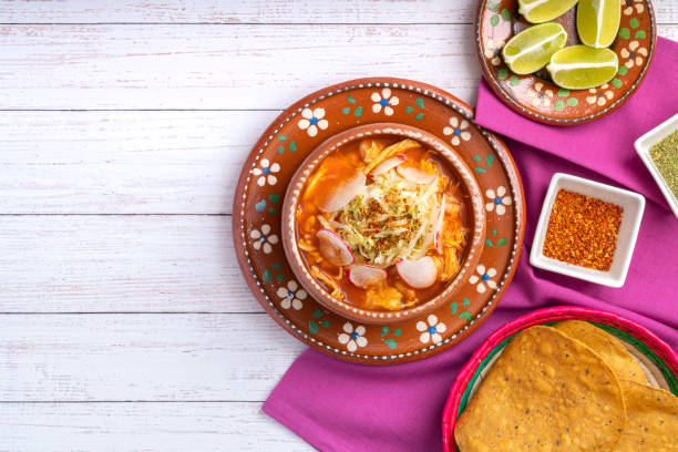 comida tradicional mexicana. sopa de pozole rojo con pollo acompañada de aguacate, lechuga, cebolla, rábano, limón, chile y tortillas crujientes de maíz también conocidas como tostadas sobre fondo de madera blanca. - guacamole restaurant mexican cuisine avocado fotografías e imágenes de stock