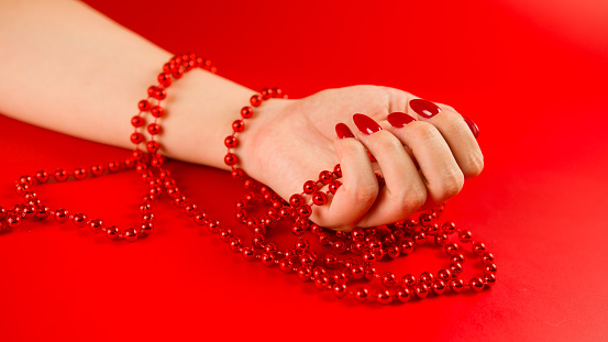 From above of crop anonymous woman with red beads and with red manicure on red background in studio.