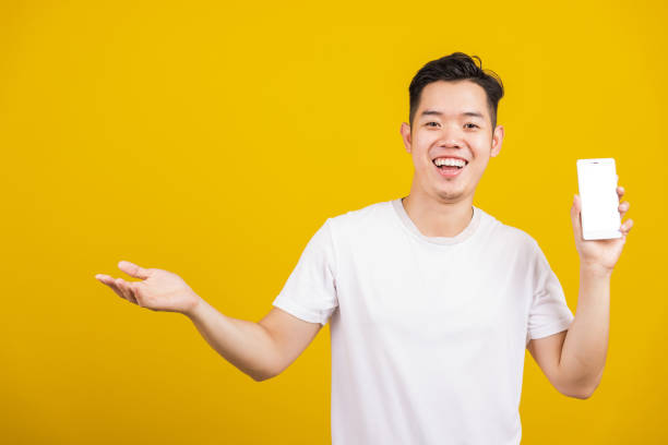 istock Asian handsome young man smiling positive showing mobile phone blank screen with another hand palm open empty space, excited happy male hold smartphone studio shot isolated on yellow background 1371873323