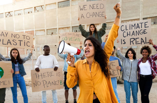 woman with arm raised shouting through megaphone lead demonstration against global warming. protesters hold signs - placard women holding standing imagens e fotografias de stock