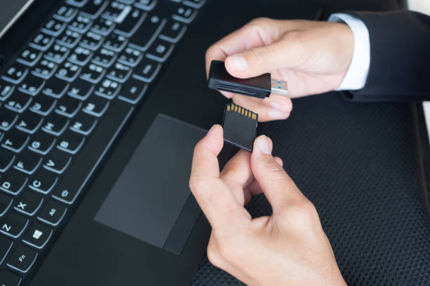 Hand with black suit holding memory sd card and card reader for copy data from camery to laptop computer