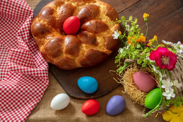 Easter Greek tsoureki braid top view. Sweet bread brioche and colorful egg on wood, checked red tablecloth background