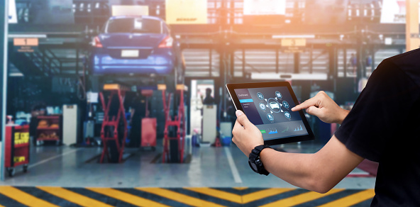 Mechanic using digital tablet Inspecting the Vehicle with auto repair shop as background