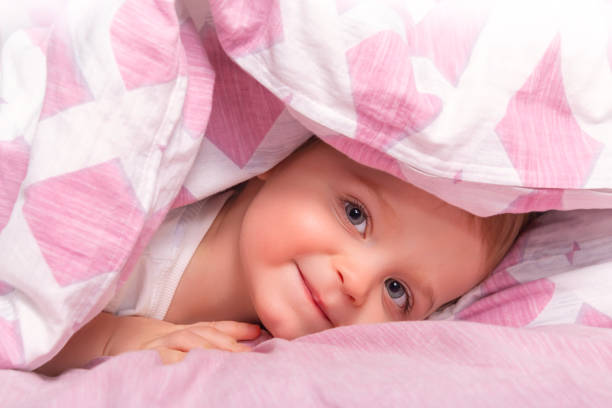 Adorable caucasian baby boy hidding under blanket and playing heed and seek. Happy child. Pink blanket. Looking to the camera.