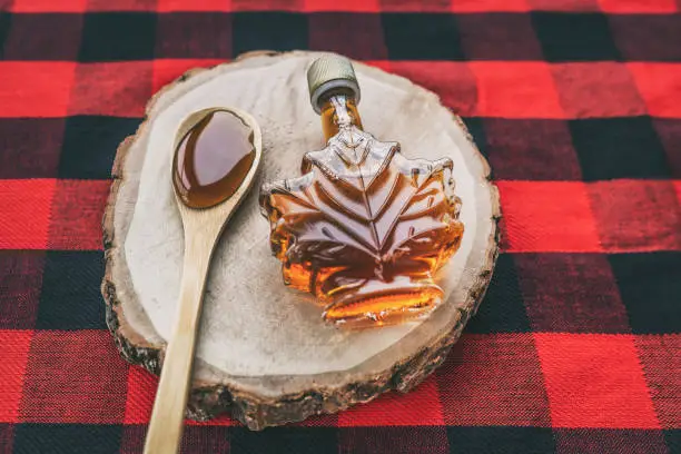 Photo of Maple syrup bottle Quebec cultural food traditional harvest top view on buffalo dining tablecloth background. Canada grade A amber sweet liquid in wooden spoon from sugar shack cabane a sucre farm