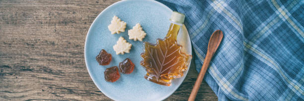 Maple syrup bottle and pure soft sugar candy and taffy top view on kitchen table panoramic banner. Cooking ingredient for dessert recipe, traditional food from Quebec wood rustic plate panorama. stock photo