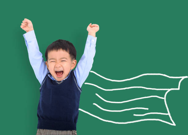 Happy asian kid against green blackboard with superhero and knowledge is power concept stock photo