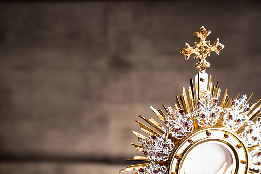 Catholic symbols composition. The Cross, monstrance,  Holy Bible and golden chalice on wooden altar and gray background.