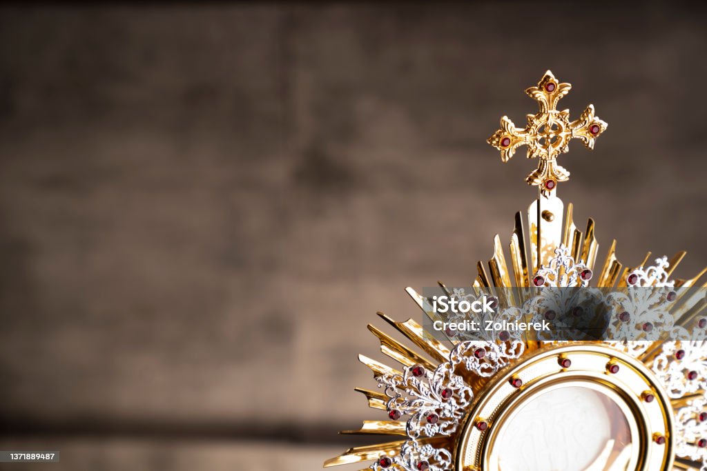 Catholic religion concept. Catholic symbols composition. The Cross, monstrance,  Holy Bible and golden chalice on wooden altar and gray background. Catholicism Stock Photo