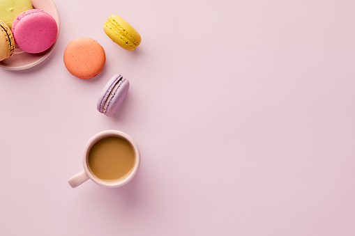 Colorful delicious French dessert macaron or macaroons with a coffee cup on pink background. Top view with copy space.