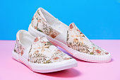 Pair of female's new stylish slip-ons with floral ornament on a pink-blue background. Close up