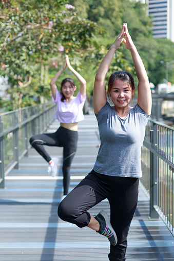 Asian women doing yoga pose and smiling to camera in the outdoor city park