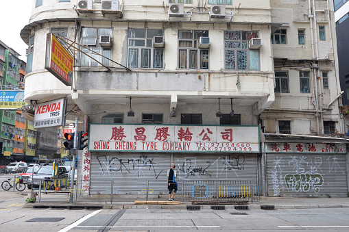 Man walking on a sidewalk by a closed tyre center in To Kwa Wan, an area of the eastern shore of Kowloon peninsula. The area belongs to the Kowloon City District of Kowloon. It's a mixed residential and commercial area, and is located to the west of the old Kai Tak Airport.