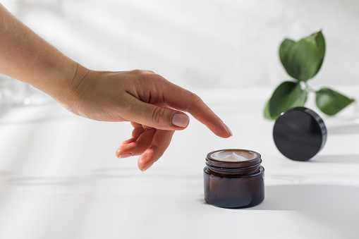 A woman's hand reaches for a jar of nourishing skin cream on a white background with a shadow pattern. High quality photo