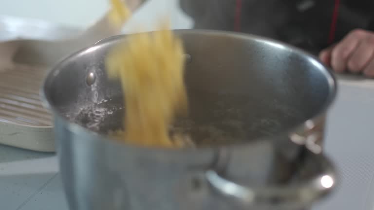 Bowtie pasta being poured into a stainless steel pot with boiling water