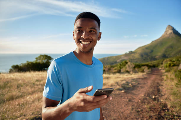 흑인 젊은 성인 남성은 그의 산 실행에 나가는 동안 미소. 손에 자신의 휴대 전화를 들고, 타이머를 설정하려고 - ewan 뉴스 사진 이미지