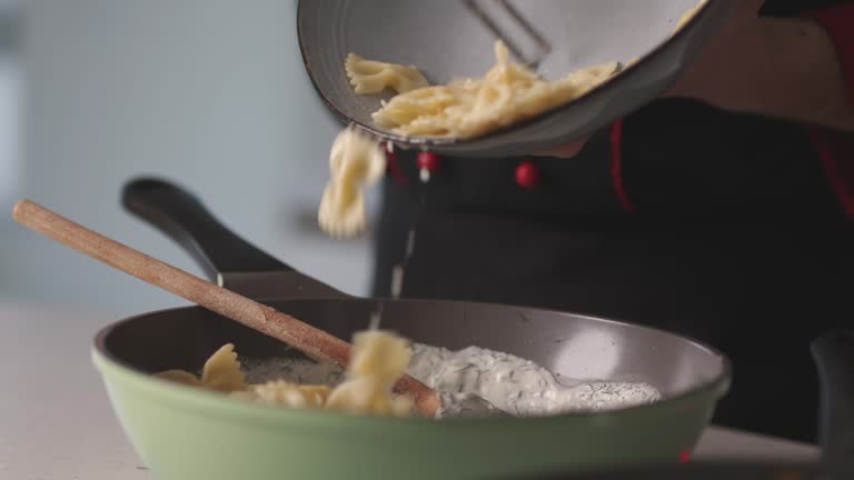 Chef using kitchen tweezers and pouring cooked bowtie pasta into a sauce