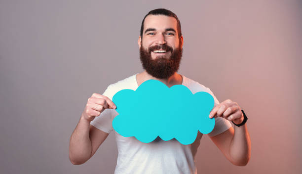 istock Bearded man is holding a blue paper cloud in front of his chest in a studio. 1371896516
