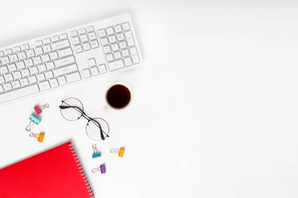 istock Top view of a modern office desk with a notepad, glasses, keyboard and a coffee or tea cup on a white background with a place for text 1371901073