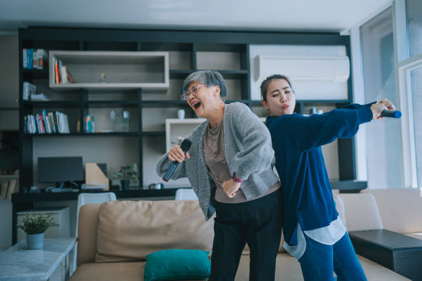 asiatisch-chinesische senior-frau, die karaoke tanzt mit ihrer tochter im wohnzimmer während der wochenend-freizeitaktivitäten - living room people joy happiness stock-fotos und bilder