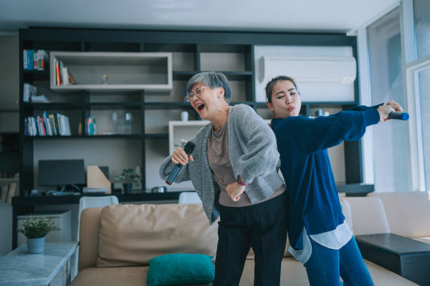 mujer asiática china mayor cantando karaoke bailando con su hija en la sala de estar durante las actividades de ocio de fin de semana - malaysian person family asian ethnicity mother fotografías e imágenes de stock