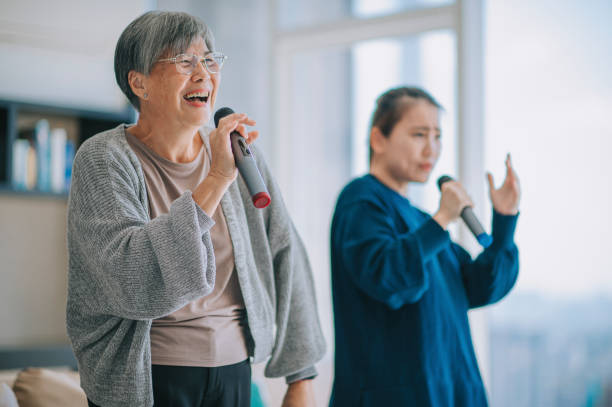 週末のレジャー活動中にリビングルームで娘とカラオケダンスを歌うアジアの中国人シニア女性 - senior adult women adult tan ストックフォトと画像