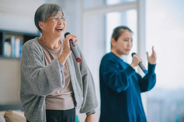 Asian Chinese Senior woman singing karaoke dancing with her daughter in living room during weekend leisure activities