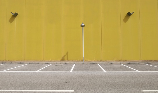 Yellow concrete wall with a streetlight in the middle. Sidewalk and asphalt road with parking in front. Background for copy space