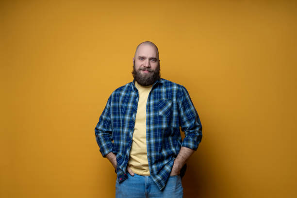 Portrait of a mature bearded male wearing plaid shirt on yellow background. Happy man looking at camera isolated over yellow wall with copy space. Close up face of happy successful self-confident man. Portrait of a mature bearded male wearing plaid shirt on yellow background. Happy man looking at camera isolated over yellow background with copy space. Close up face of happy successful self-confident man. man beard plaid shirt stock pictures, royalty-free photos & images