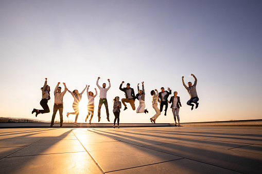 Large group of cheerful business people having fun while jumping on a terrace at the rooftop. Copy space.