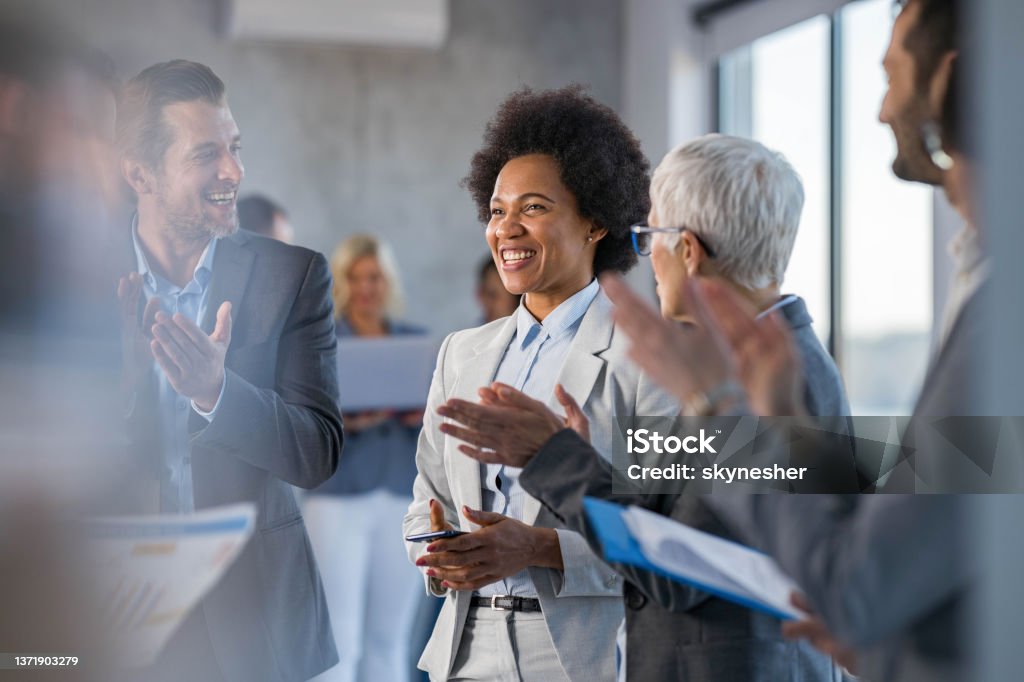 Happy business colleagues applauding in a hallway full of people. Happy entrepreneurs applauding to their African American colleague in a full hallway. Congratulating Stock Photo