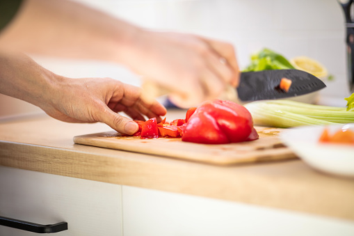 Unrecognizable man chopping tomato and red bell pepper on wooden cutting board