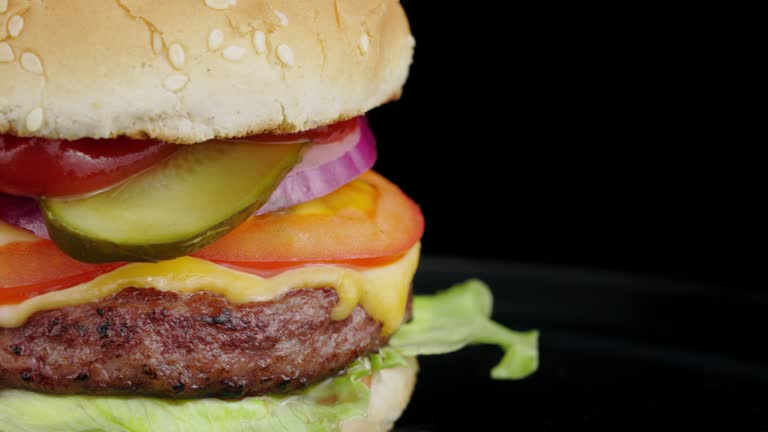 Beef burger rotating 360 loop on the black plate on black background, close-up.