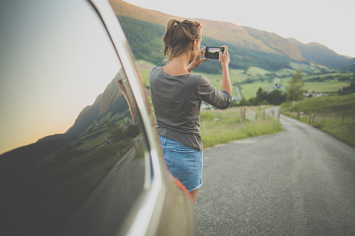 Traveling in nature, woman photographing alpine landscape with her smartphone