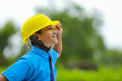 Cute Asian Indian little child wearing yellow construction helmet or safety hard hat.