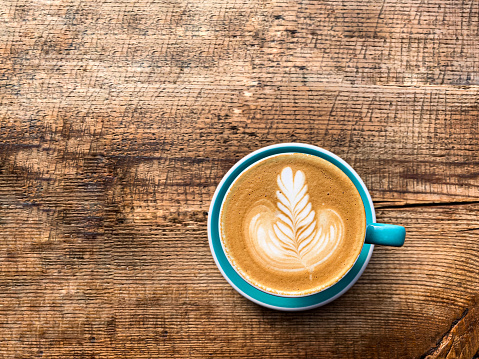 A mug of flat white coffee on a wooden background. Coffee art. Heart flower shape latte art. Turquoise cup and saucer