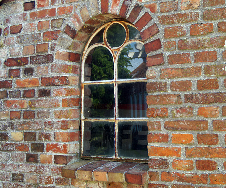 The window of a stable near an old mill. It has an arch and glass panels. The iron frame is a bit rusted. Location:  Neuharlingersiel, East Friesland, Germany