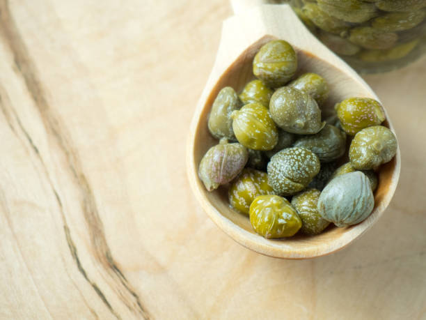 istock Pickled or marinated green capers on a wooden spoon close up, selective focus 1371916023