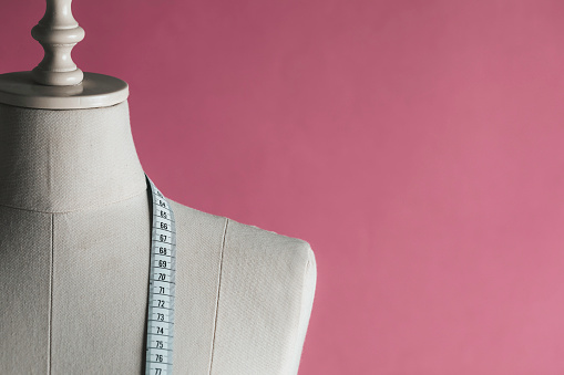 Tailor Mannequin with measure tape in front of pink background.