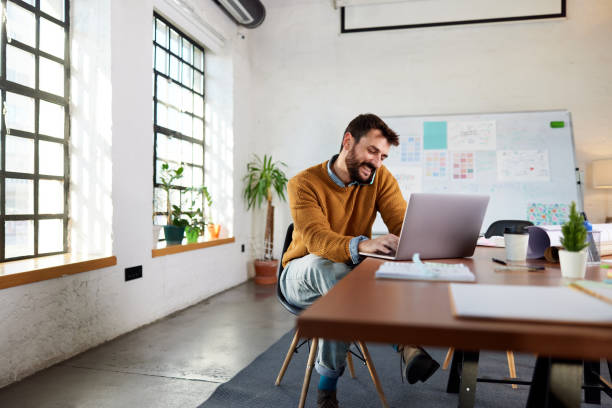 istock Happy freelancer talking on cell phone while using laptop at casual office. 1371919249